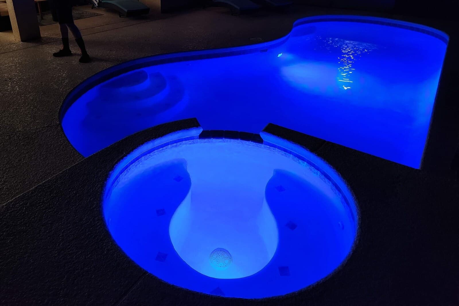 Private spa glowing blue at night beside the pool